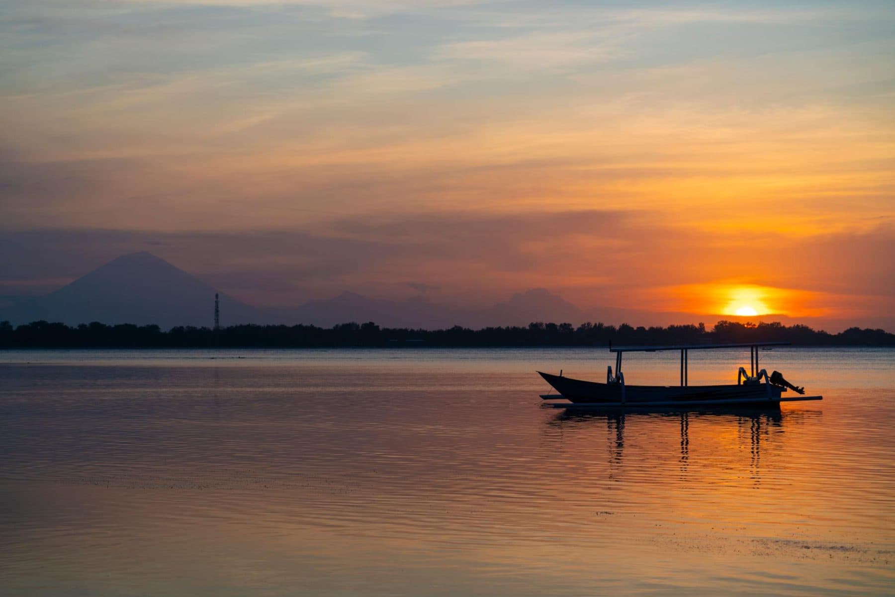 Boat on calm water at sunset with the mountain silhouette