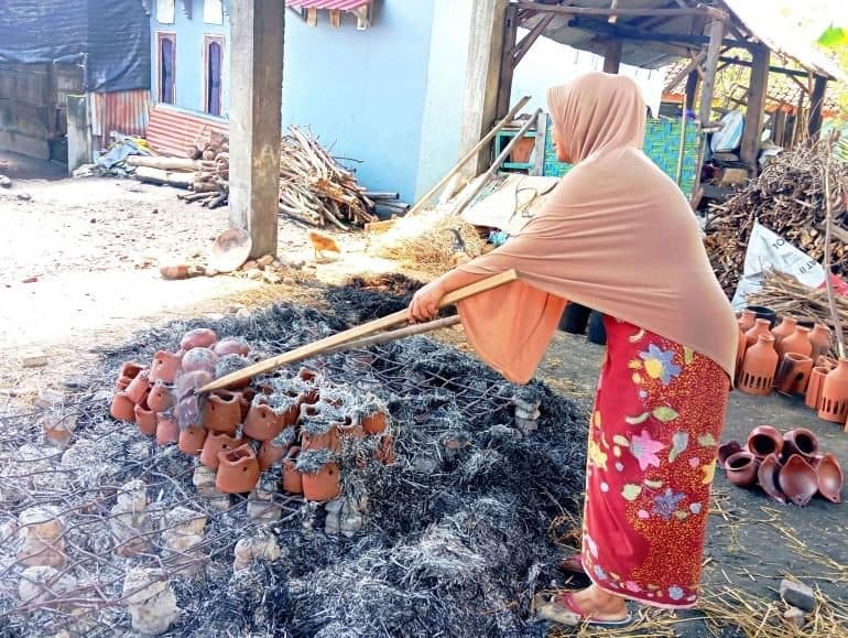 Firing clay pots over straw and ash in a Banyumulek yard