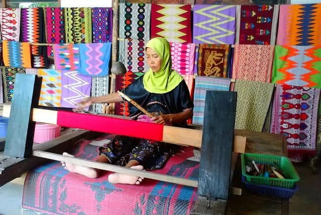 A weaver in a workshop lined with colorful ikat fabrics