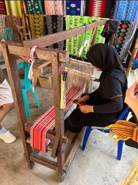 A weaver at a wooden loom with striped fabric in Sukarara