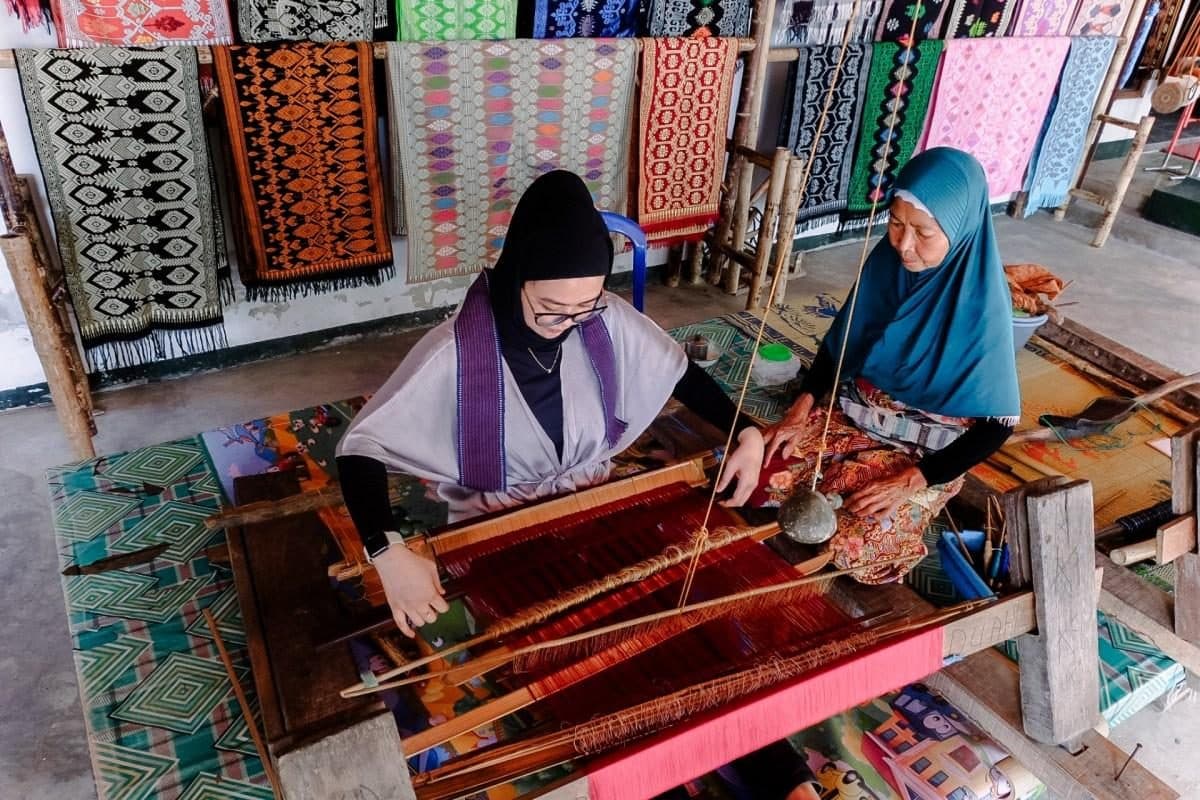A visitor learning traditional weaving beside a Sukarara artisan