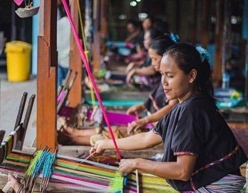 Weavers in a row working bright threads on traditional looms