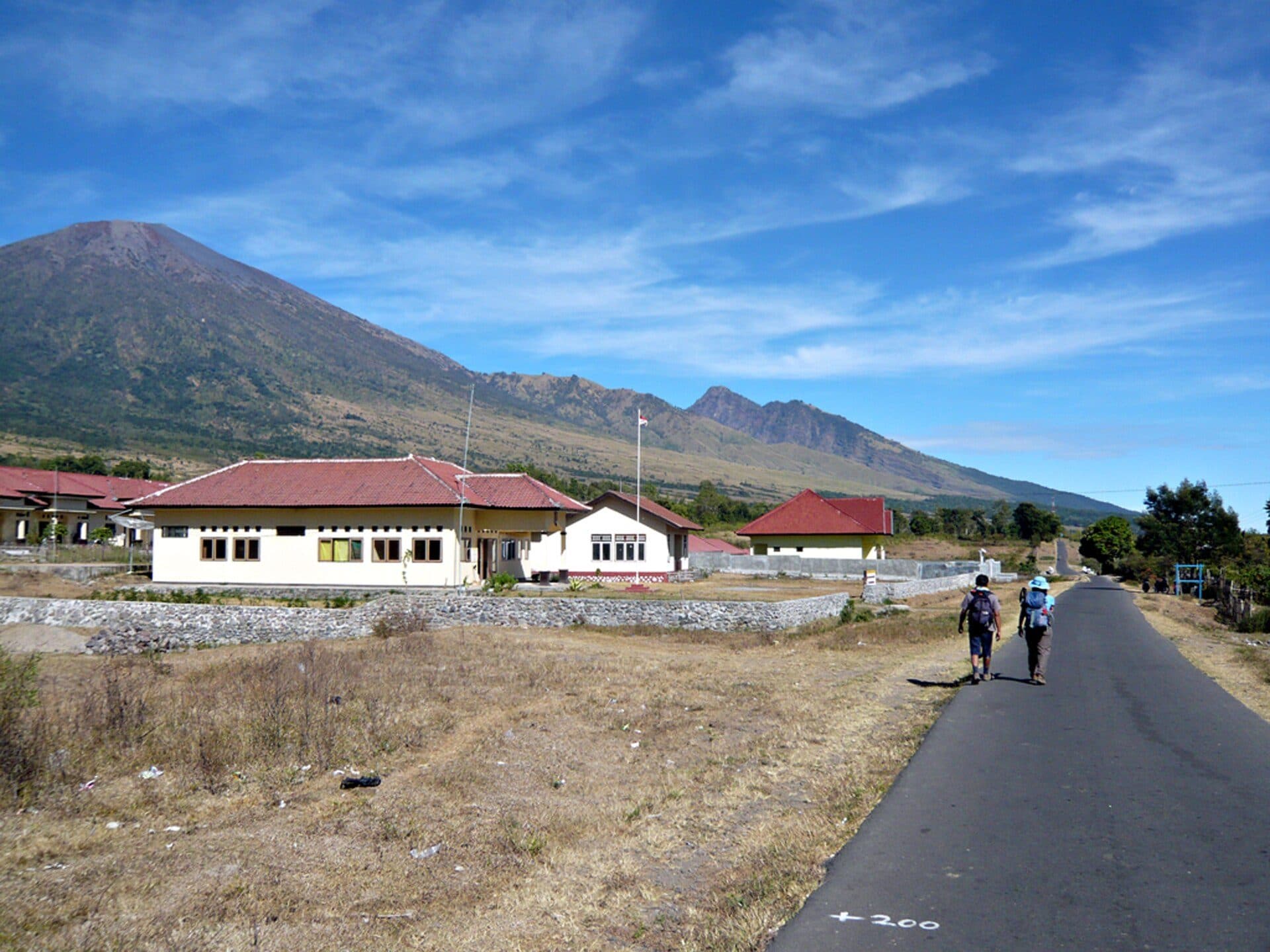Walkers on the road through Sembalun Lawang with Rinjani behind the village
