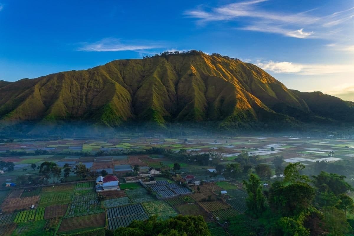 Sunrise light on a Sembalun mountain above misty valley farms