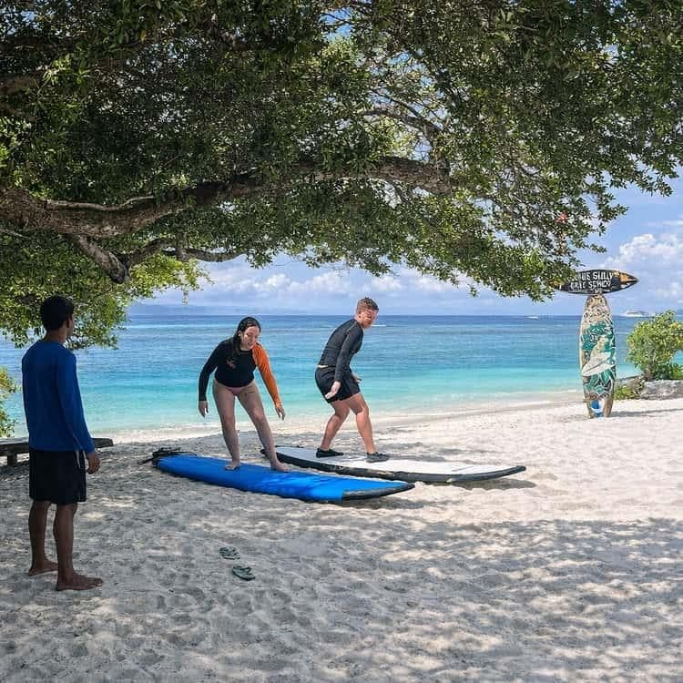 A beach surf lesson under trees facing turquoise Gili water
