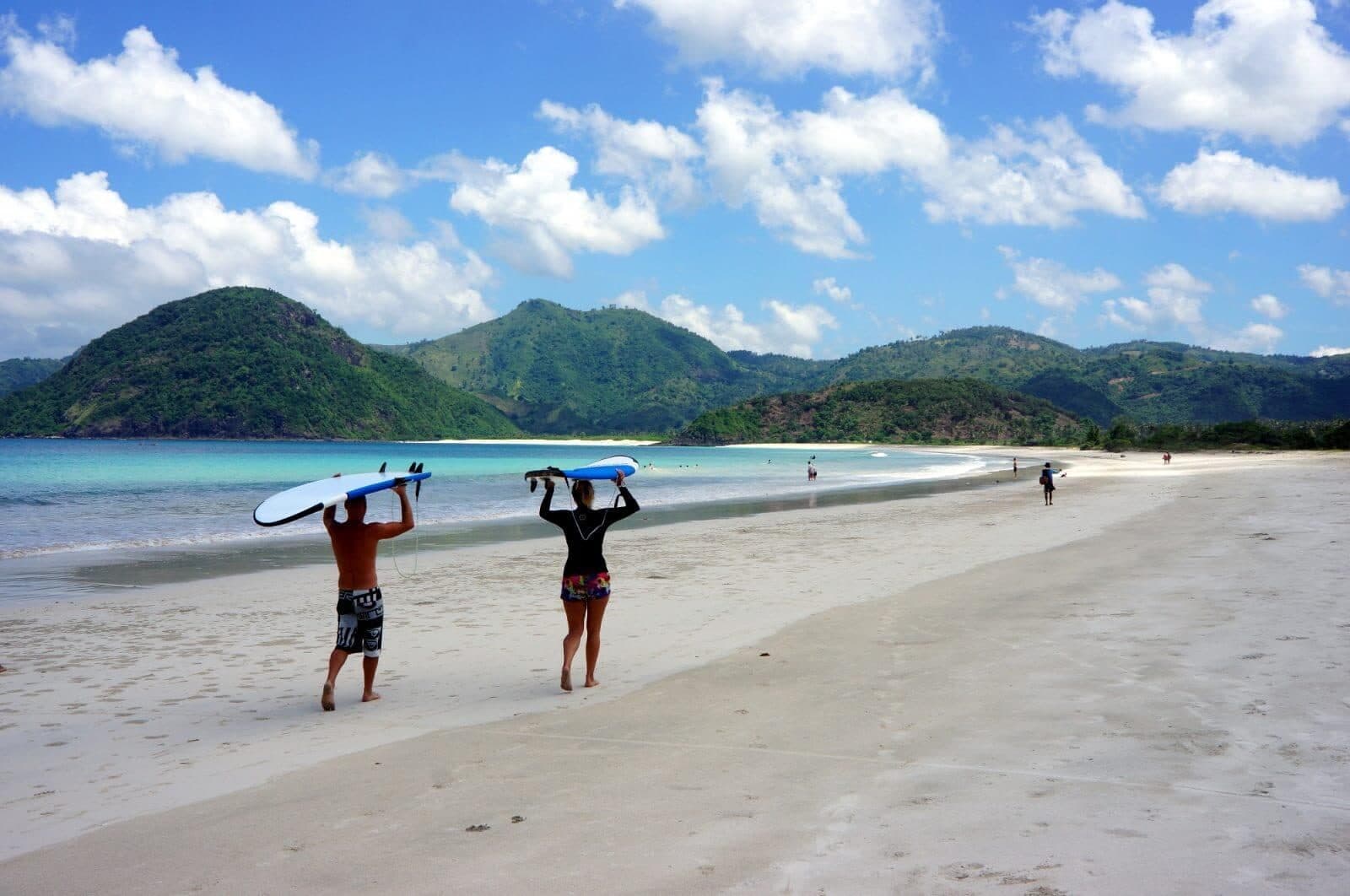Two surfers carrying boards along Selong Belanak's crescent beach
